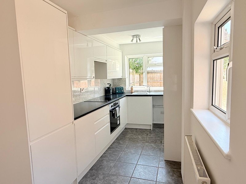 Modern kitchen with white cabinets, black countertop, built-in appliances and tiled floor