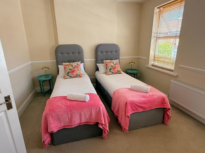 Twin bedroom with two single beds, pink throws, floral cushions, and window with blinds