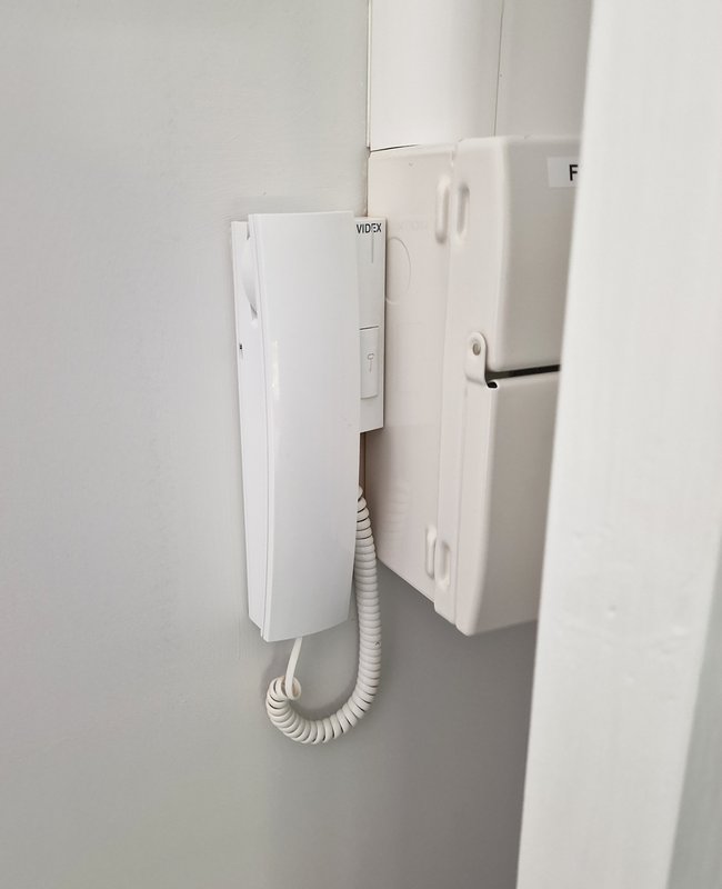 White wall-mounted intercom or entry phone system with coiled cable