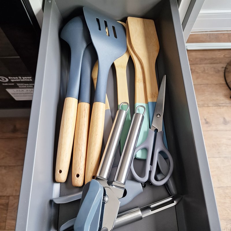 Kitchen drawer with organized cooking utensils including wooden-handled spatulas, scissors, and metal kitchen tools