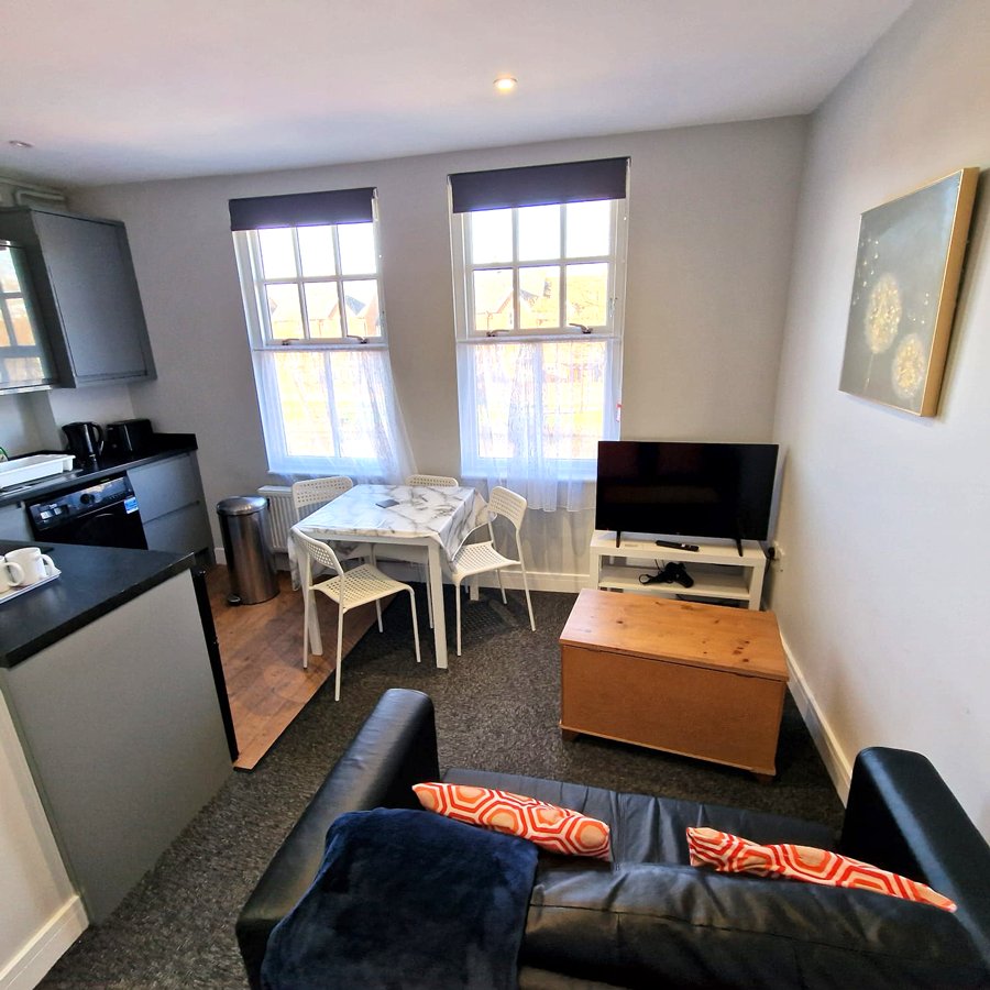 Open-plan living area with kitchen, dining table, sofa, TV and large windows