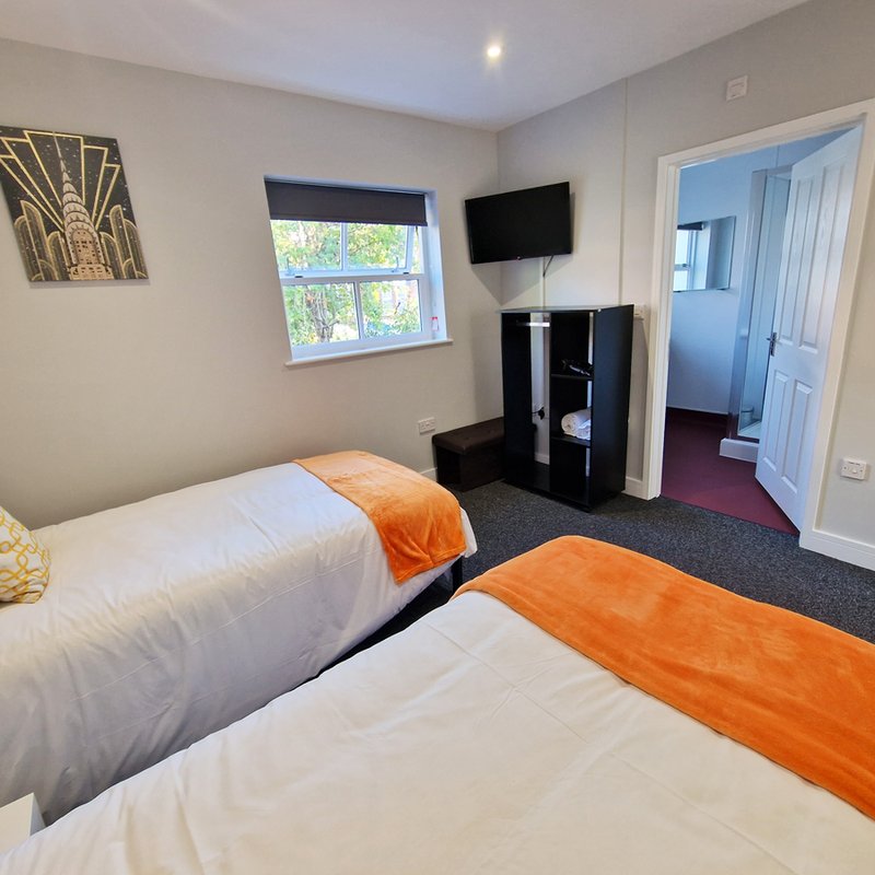 Modern bedroom with two single beds, orange throws, wall-mounted TV and black furniture unit