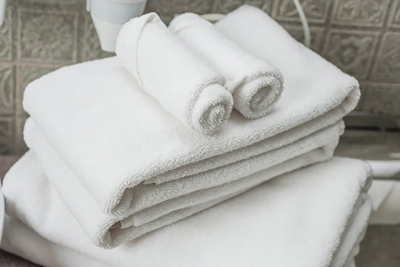 Stack of white rolled and folded towels on bathroom shelf