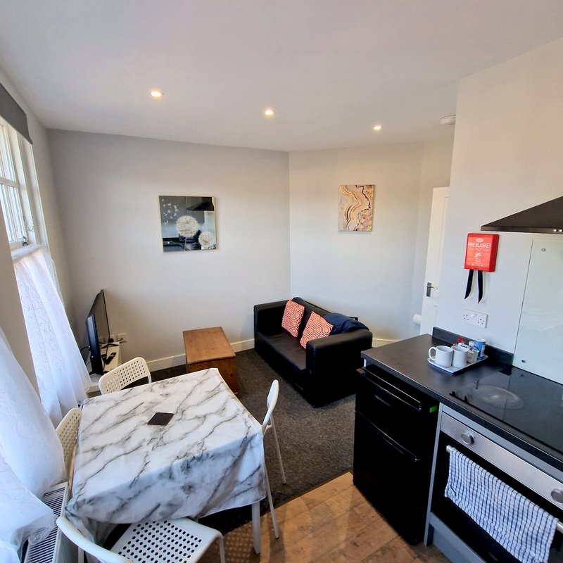 Open-plan studio apartment with dining table, black sofa, kitchen area and window