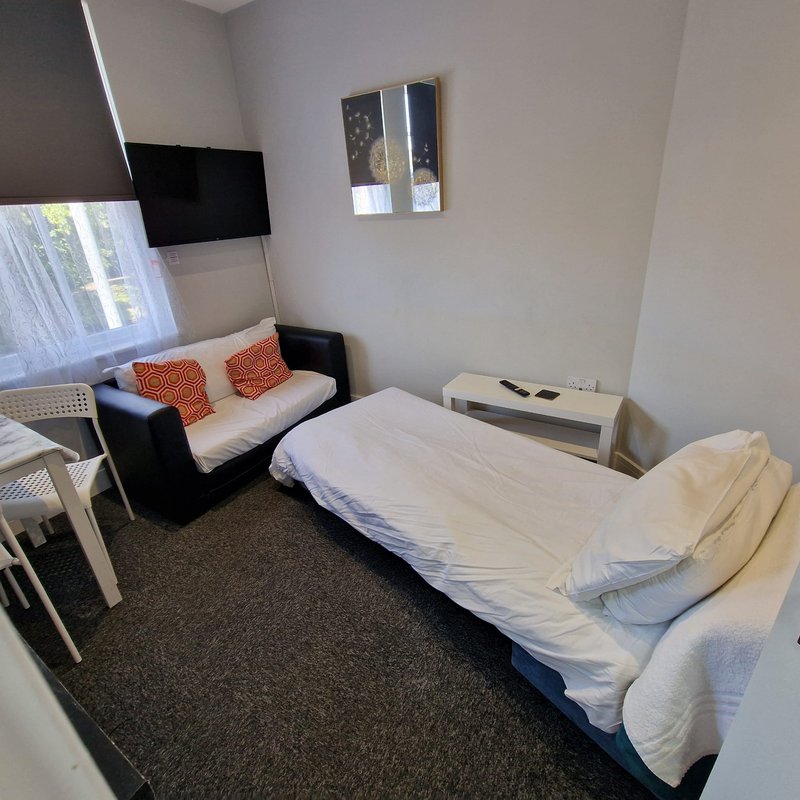 Compact bedroom with single bed, sofa seating, TV, and window with natural light