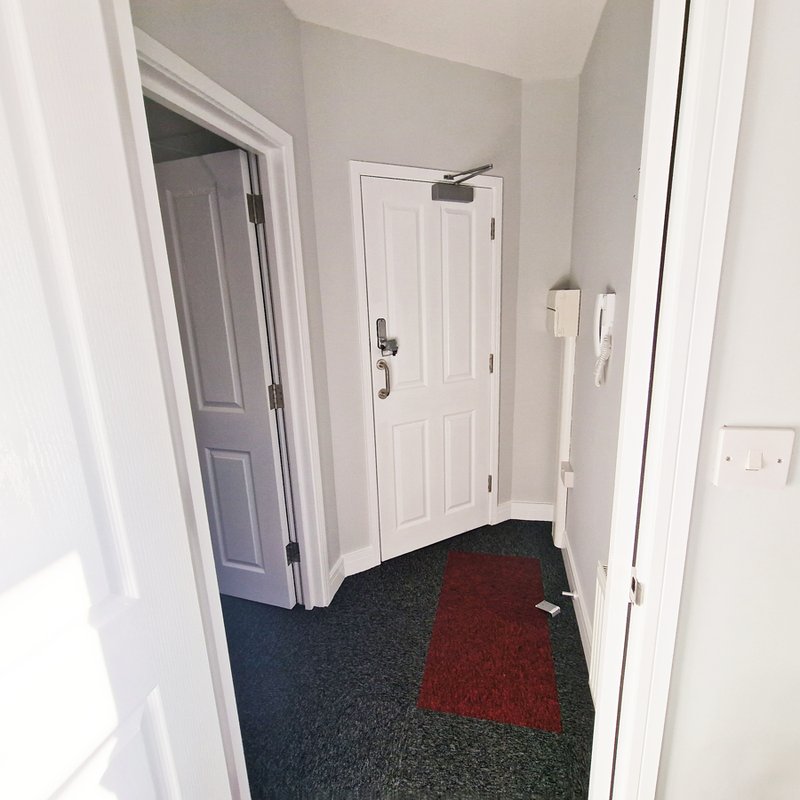Hallway with white walls, multiple doors, and geometric patterned carpet in navy and burgundy