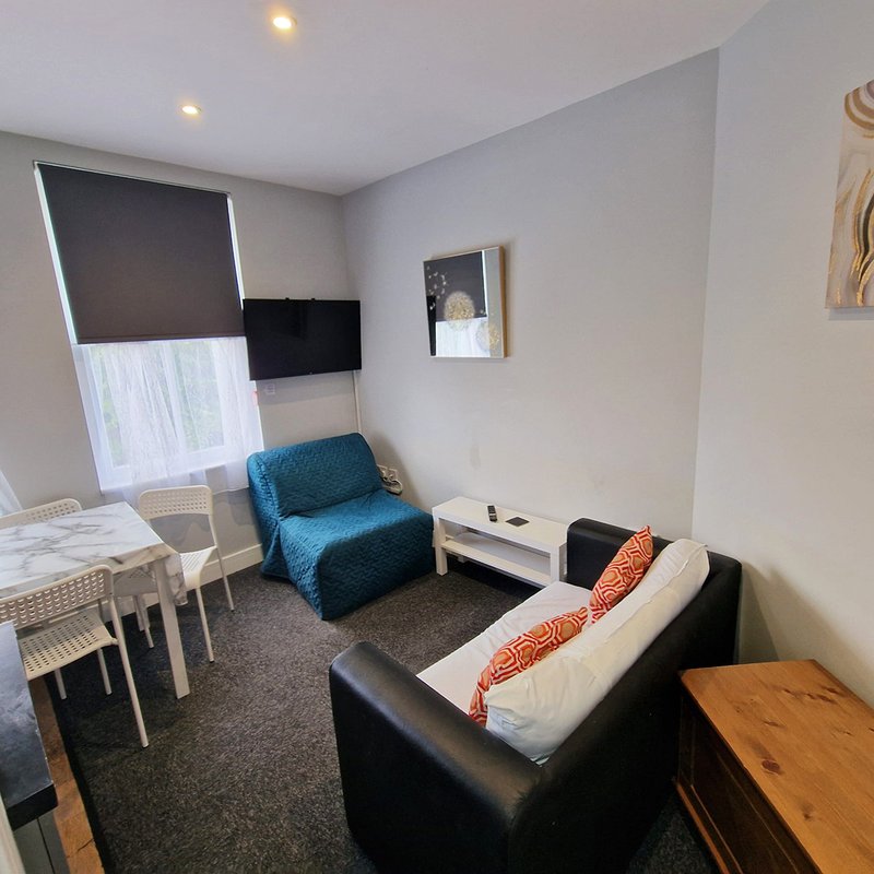 Modern bedroom with black leather sofa, blue armchair, TV, dining table and recessed ceiling lights