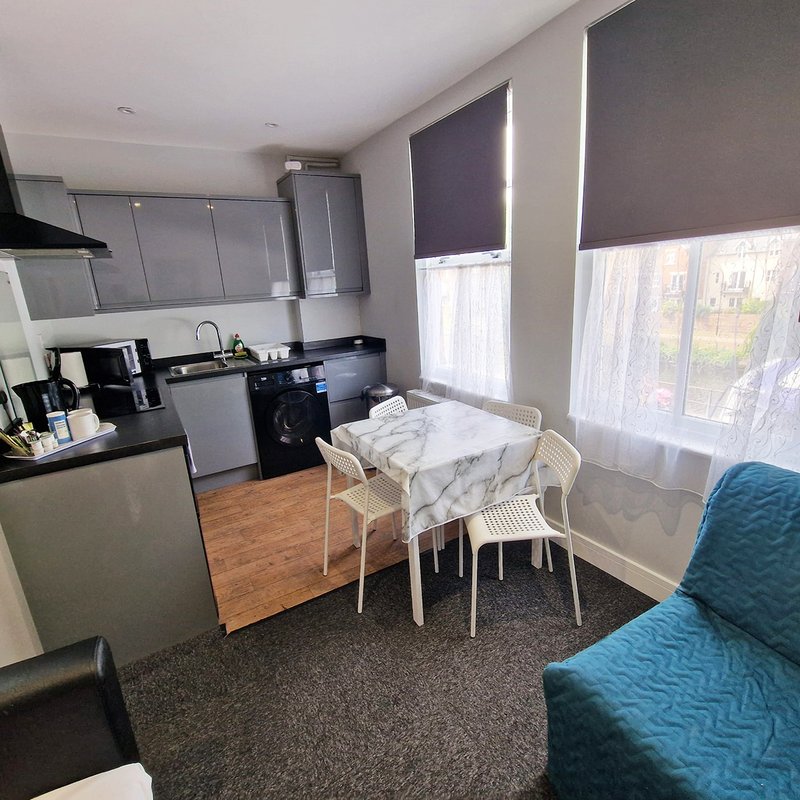Open-plan kitchen and living area with dining table, blue sofa, and large windows