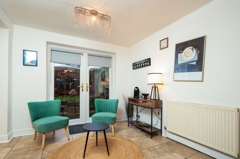 Modern living room with two teal armchairs, wooden desk, glass doors and framed wall art