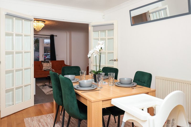 Dining room with wooden table, green upholstered chairs, place settings, and open-plan view to lounge