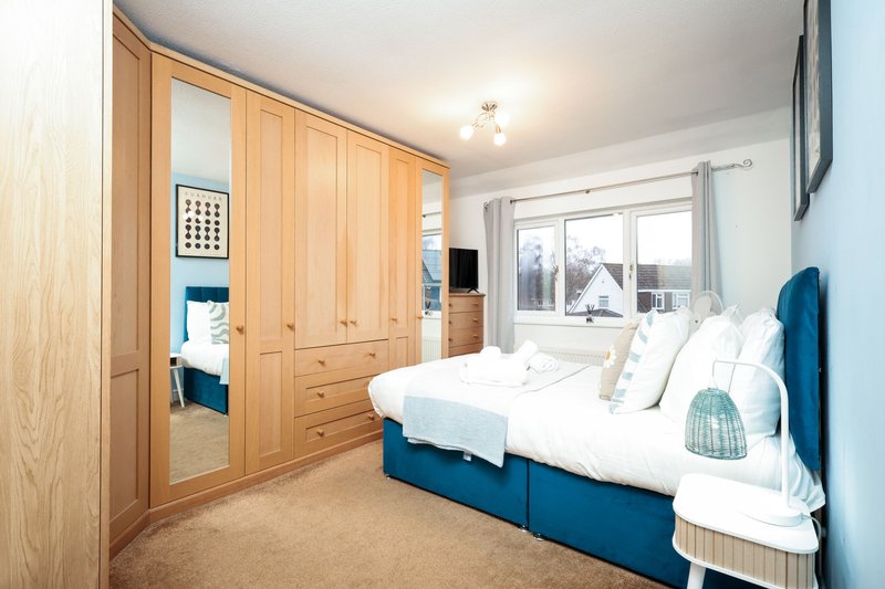 Bright bedroom with double bed, blue headboard, wooden wardrobe and large window view