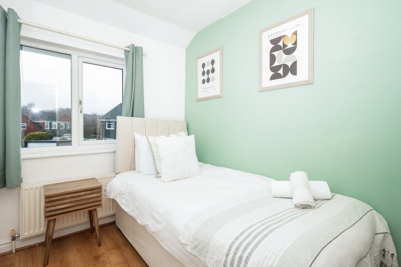 Bright bedroom with single bed, green accent wall, wooden nightstand and window