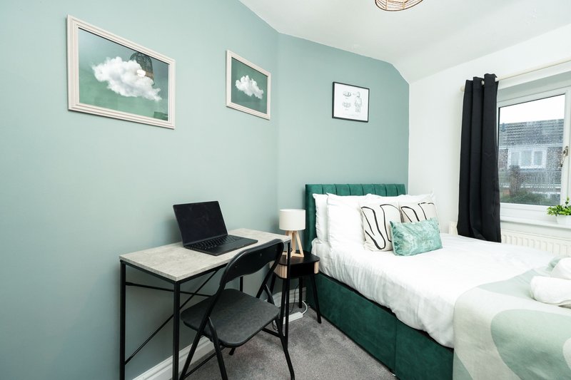 Bedroom with teal walls, double bed, desk with laptop, framed cloud artwork, and window view