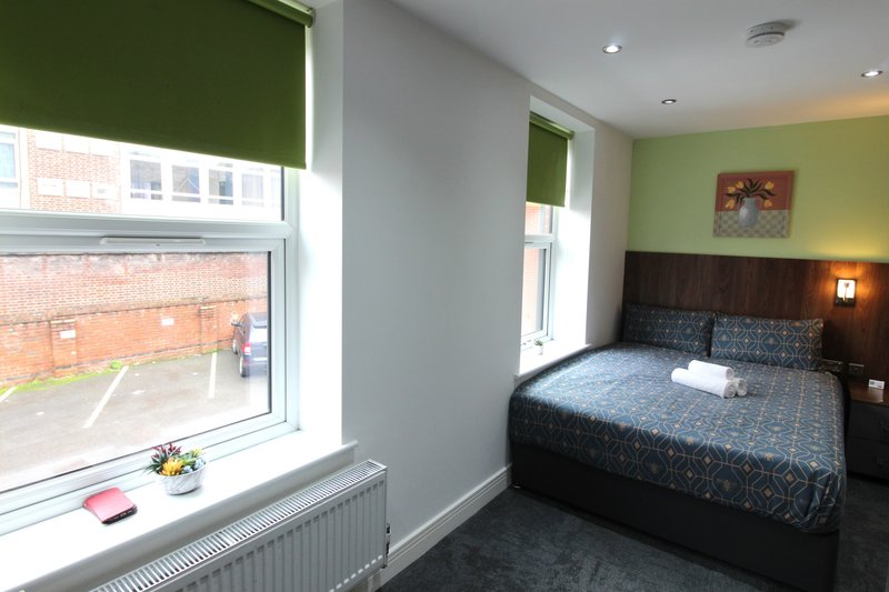Bedroom with double bed, green walls, windows overlooking street, bedside lamps