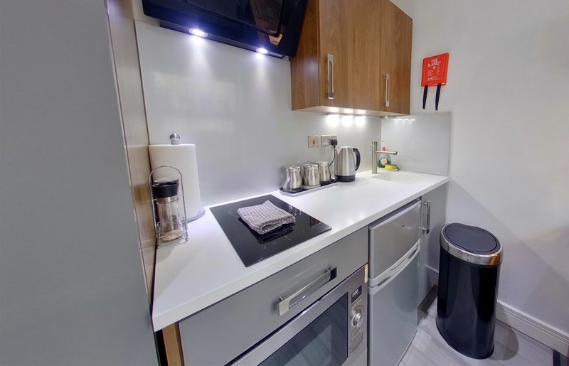 Compact kitchen with white countertop, wooden cabinets, stainless steel appliances and kettle