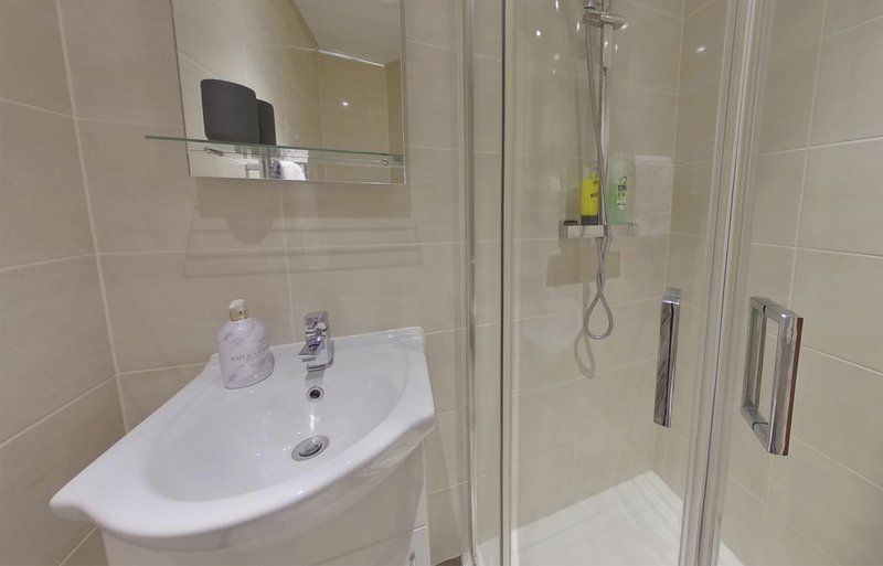 Modern bathroom with curved white sink, mirror, and enclosed shower cubicle