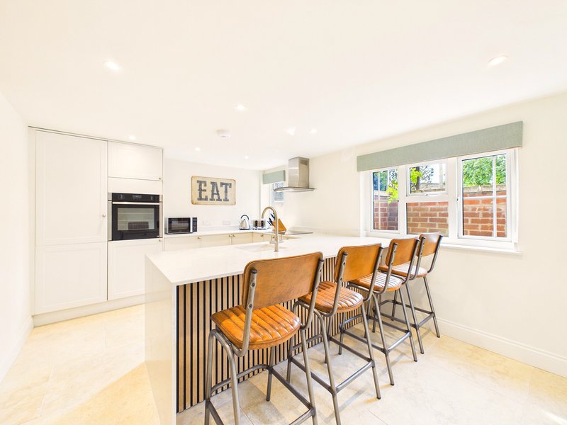 Modern kitchen with white cabinetry, island with wooden bar stools, and garden view through windows