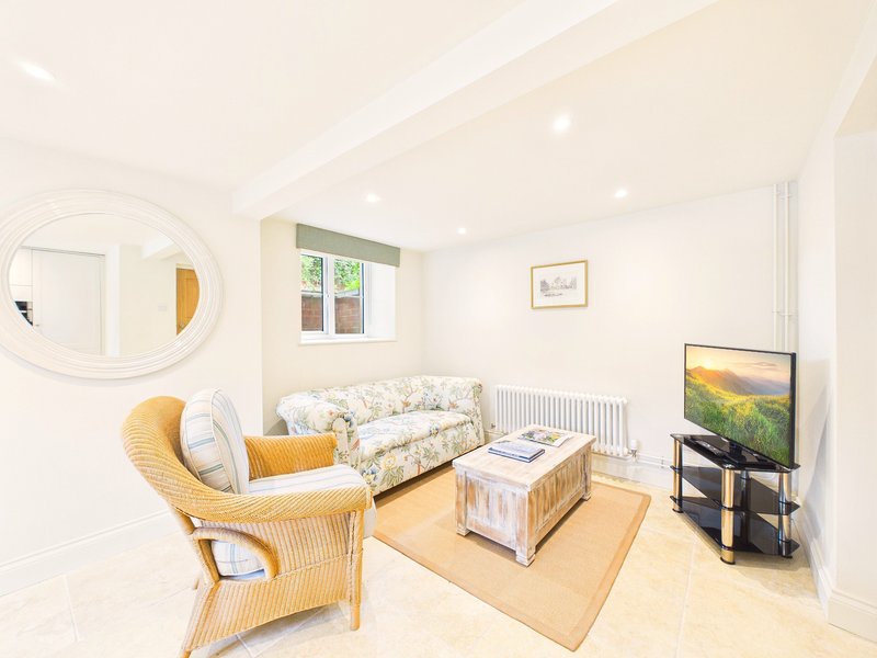 Bright living room with wicker chair, patterned sofa, TV, and round mirror