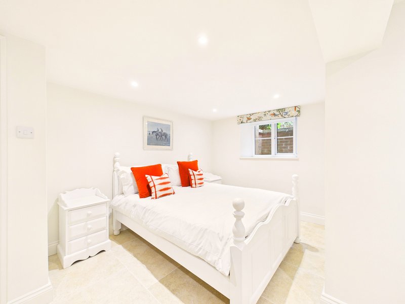 Bright bedroom with white metal bed frame, orange accent pillows, white bedding and wooden flooring