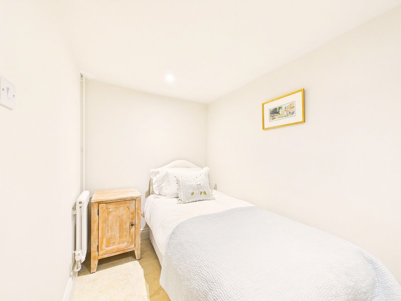 Compact bedroom with single bed, wooden nightstand, white bedding and framed wall art