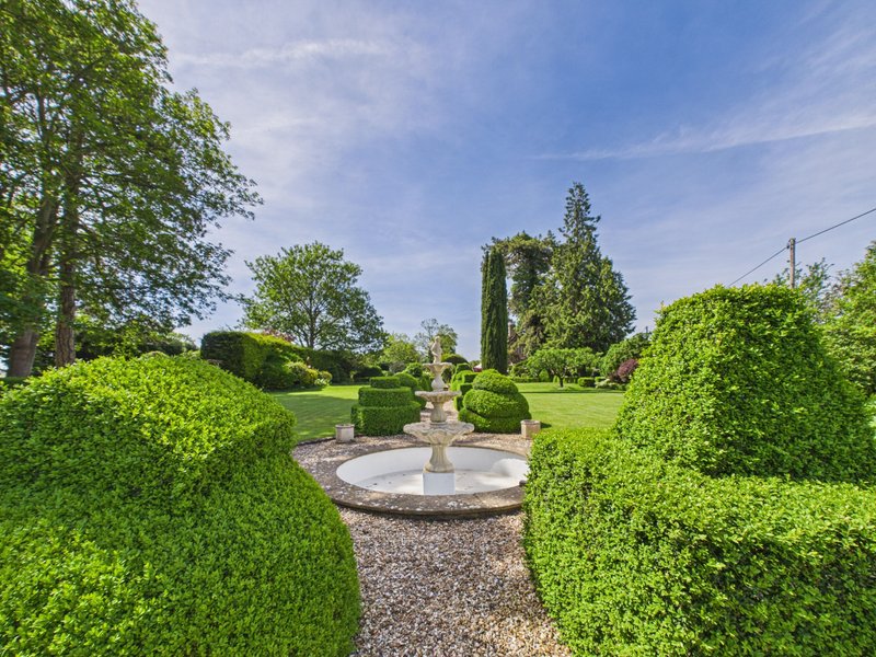 Garden with manicured hedges, central fountain, gravel path and mature trees