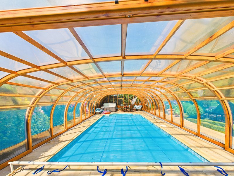 Indoor swimming pool with blue water under wooden arched polycarbonate roof structure