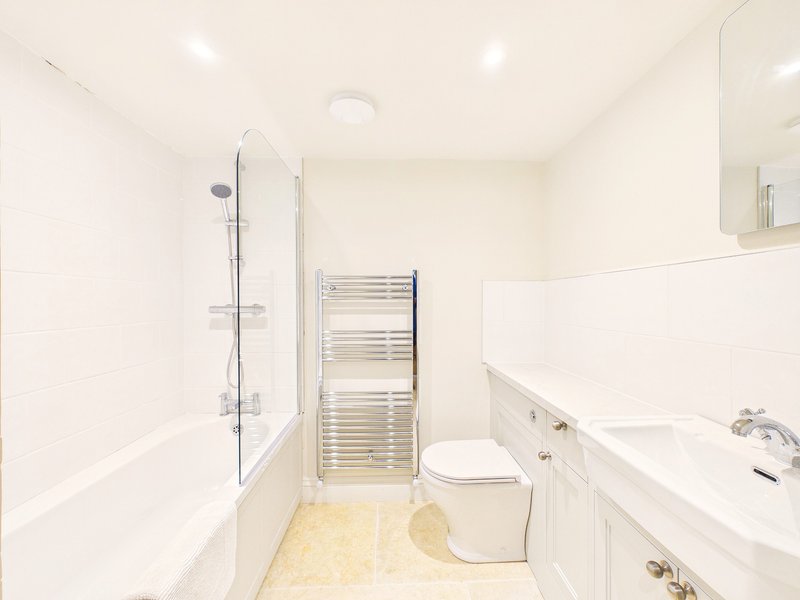 Clean modern bathroom with white subway tiles, bath with shower screen, toilet, heated towel rail and vanity sink