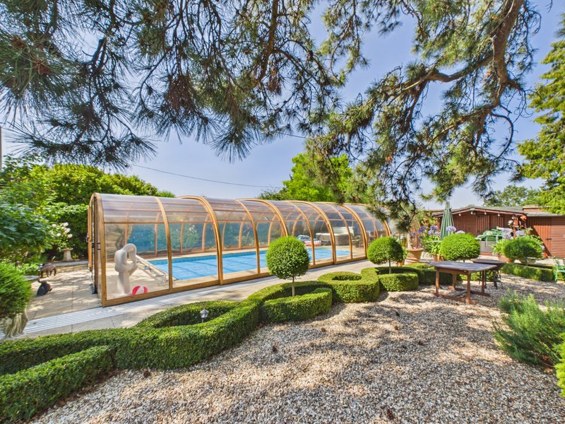 Garden with enclosed swimming pool, manicured hedges, patio seating, and mature trees overhead