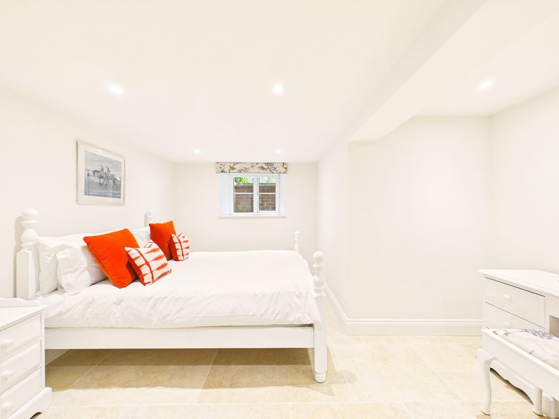 Bright bedroom with white wooden bed, orange cushions, white furniture and pale wooden flooring