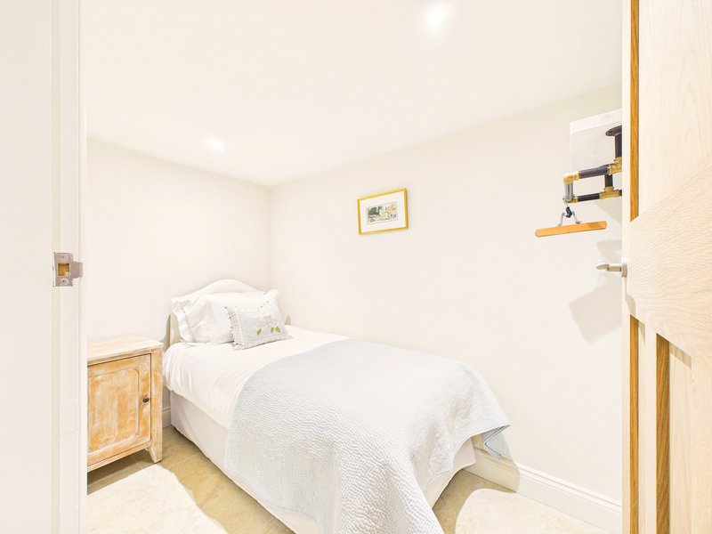 Bright bedroom with single bed, white bedding, wooden nightstand and wall shelving