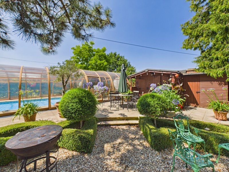 Spacious garden with pool, topiary shrubs, seating areas and greenhouse structure