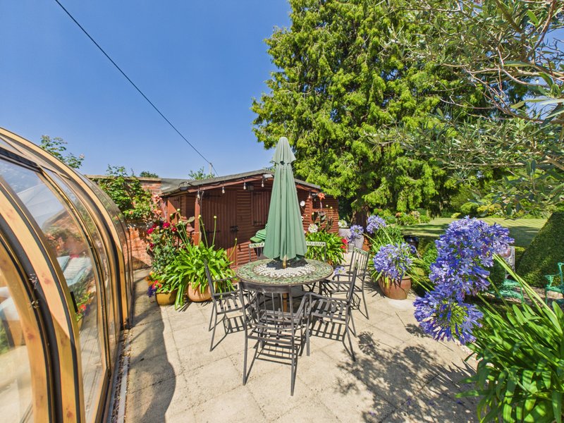 Outdoor patio with dining table, chairs, green umbrella and flowering plants