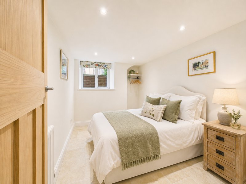 Bright bedroom with double bed, wooden door, bedside table, framed artwork and window