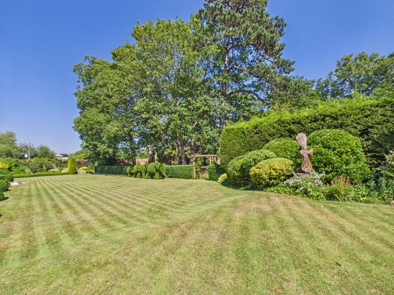 Large landscaped garden with striped lawn, mature trees and manicured hedges