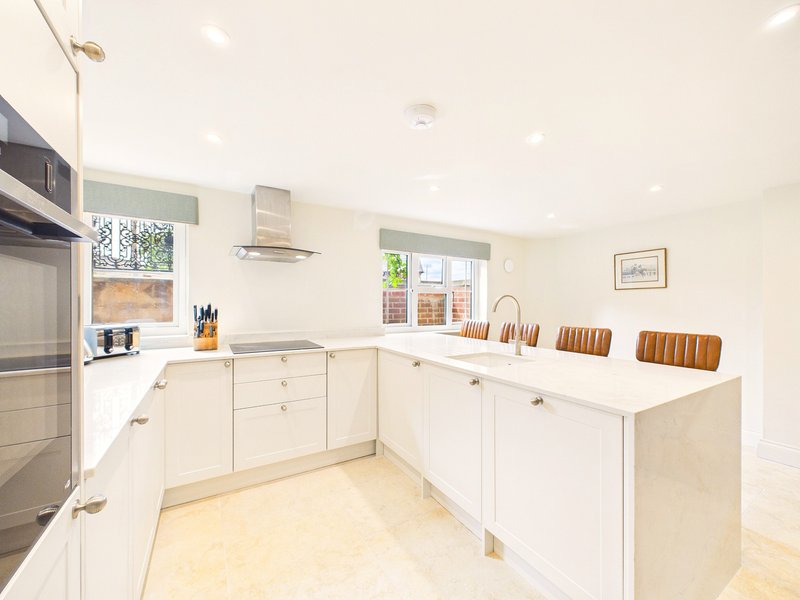Modern white kitchen with island, wooden chairs, stainless steel appliances and garden view