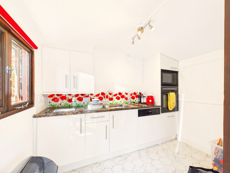 Modern white kitchen with red poppy backsplash, granite countertop, built-in appliances and tiled floor