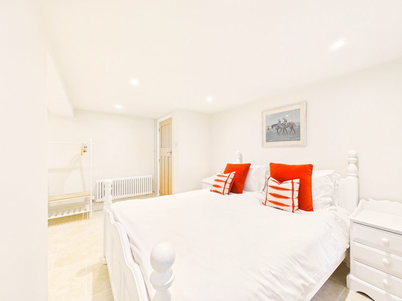 Bright bedroom with white double bed, red and white cushions, white furniture and framed artwork