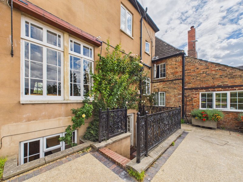 Exterior view of terraced houses with paved courtyard, ivy-covered railing, and large windows