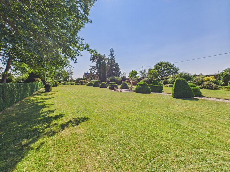 Large manicured garden with lawn, mature trees, hedges and distant house