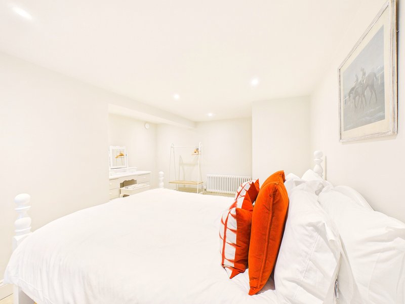 Bright modern bedroom with white bedding, orange throw, and minimalist furnishings