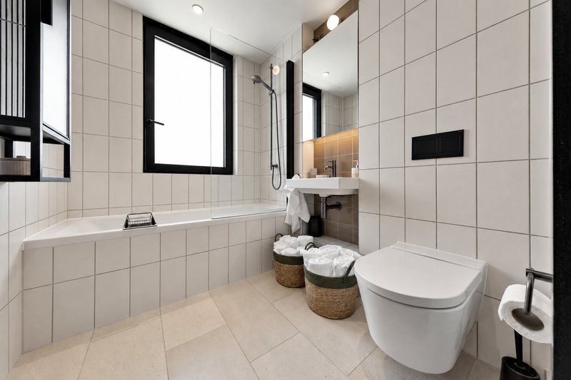 Modern bathroom with white tile walls, bathtub, toilet, vanity sink and woven storage baskets