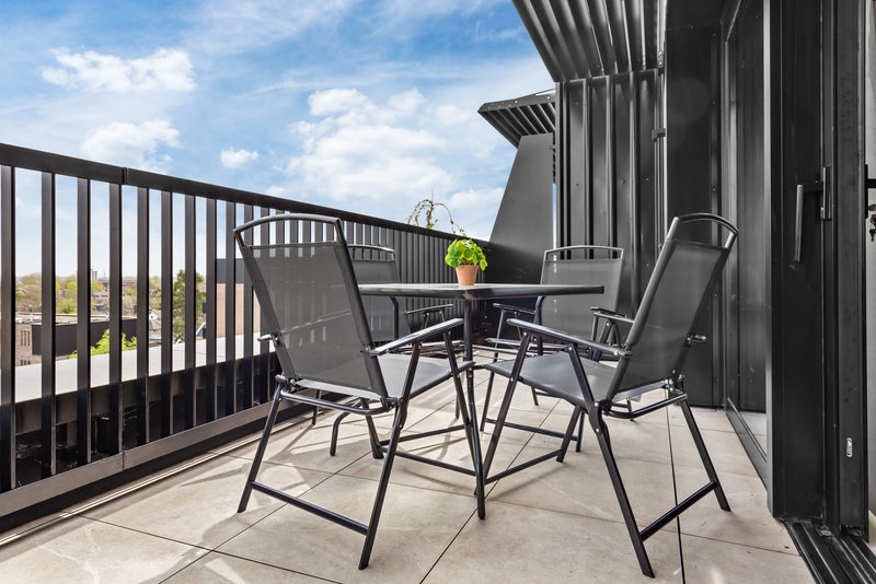 Outdoor balcony with black metal chairs, small table, and yellow flowers overlooking landscape
