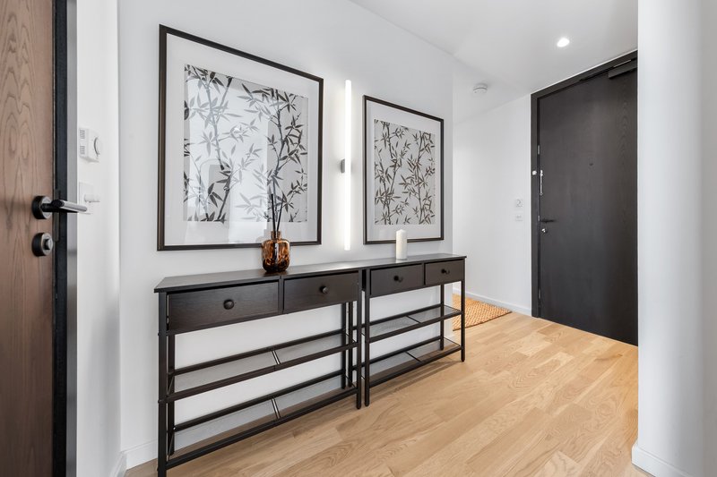 Modern entryway with black console table, framed botanical prints, wooden flooring and dark door.