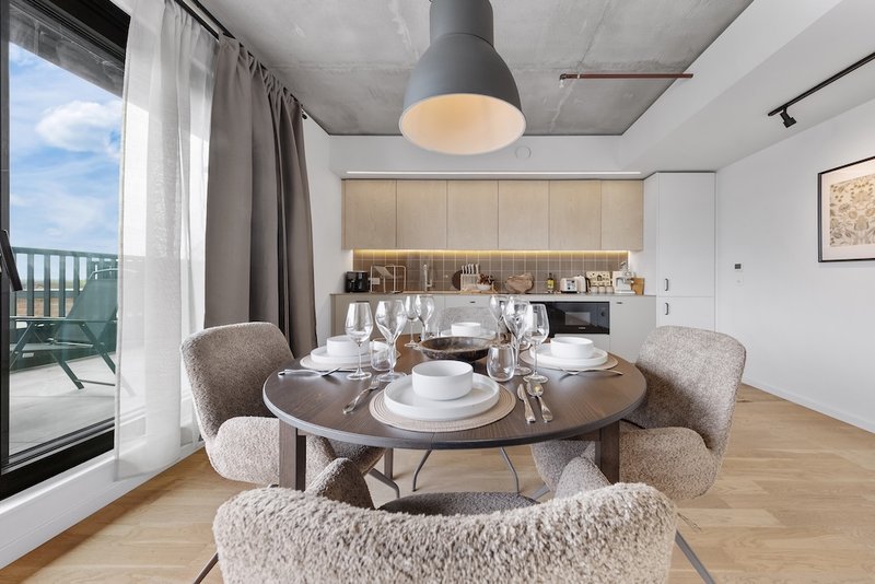 Modern dining area with round table, upholstered chairs, open kitchen and balcony view
