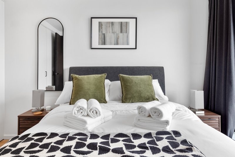 Modern bedroom with double bed, rolled towels, green cushions and arched mirror
