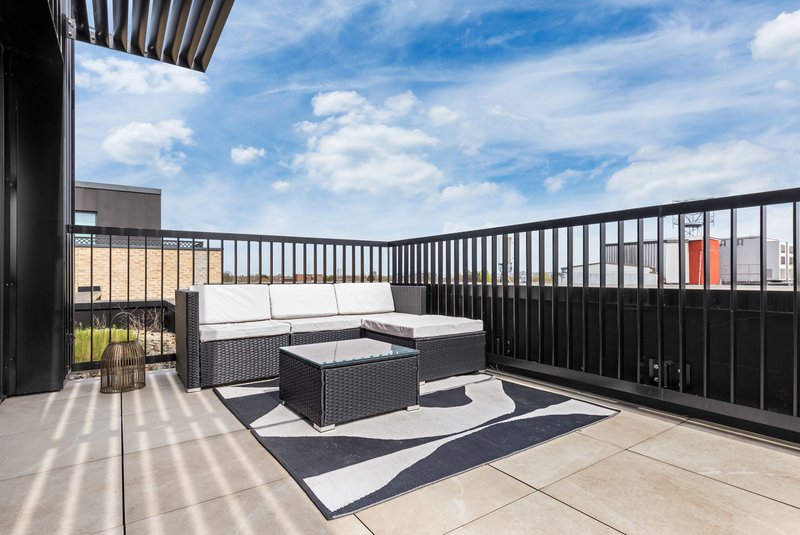 Outdoor rooftop terrace with black rattan seating, geometric rug, and city views