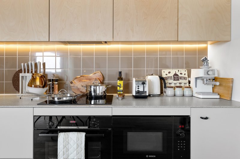 Modern kitchen with light wood cabinets, tiled backsplash, black appliances and countertop accessories.