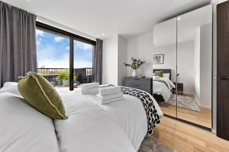 Modern bedroom with white bedding, olive cushion, mirrored wardrobe and balcony view