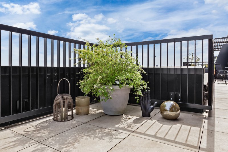 Modern rooftop terrace with black railing, potted plants, decorative lantern and sphere ornaments