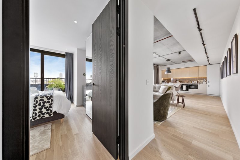 Modern open-plan apartment with light wood flooring, dark partition wall, and kitchen visible in background